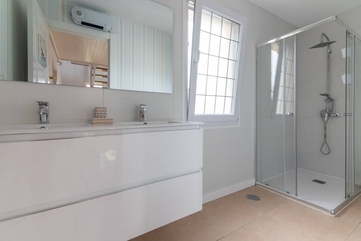 Un baño moderno con cabina de ducha de vidrio, un espejo grande y una ventana que proporciona luz natural.