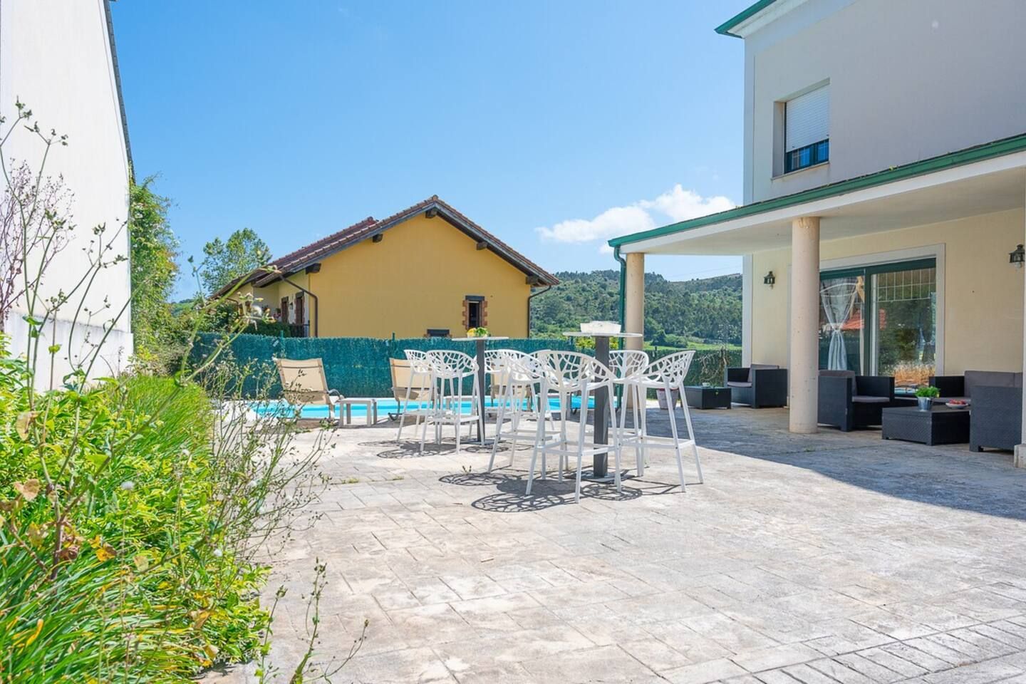 Un espace piscine avec des sièges extérieurs et une vue sur une maison jaune en arrière-plan.