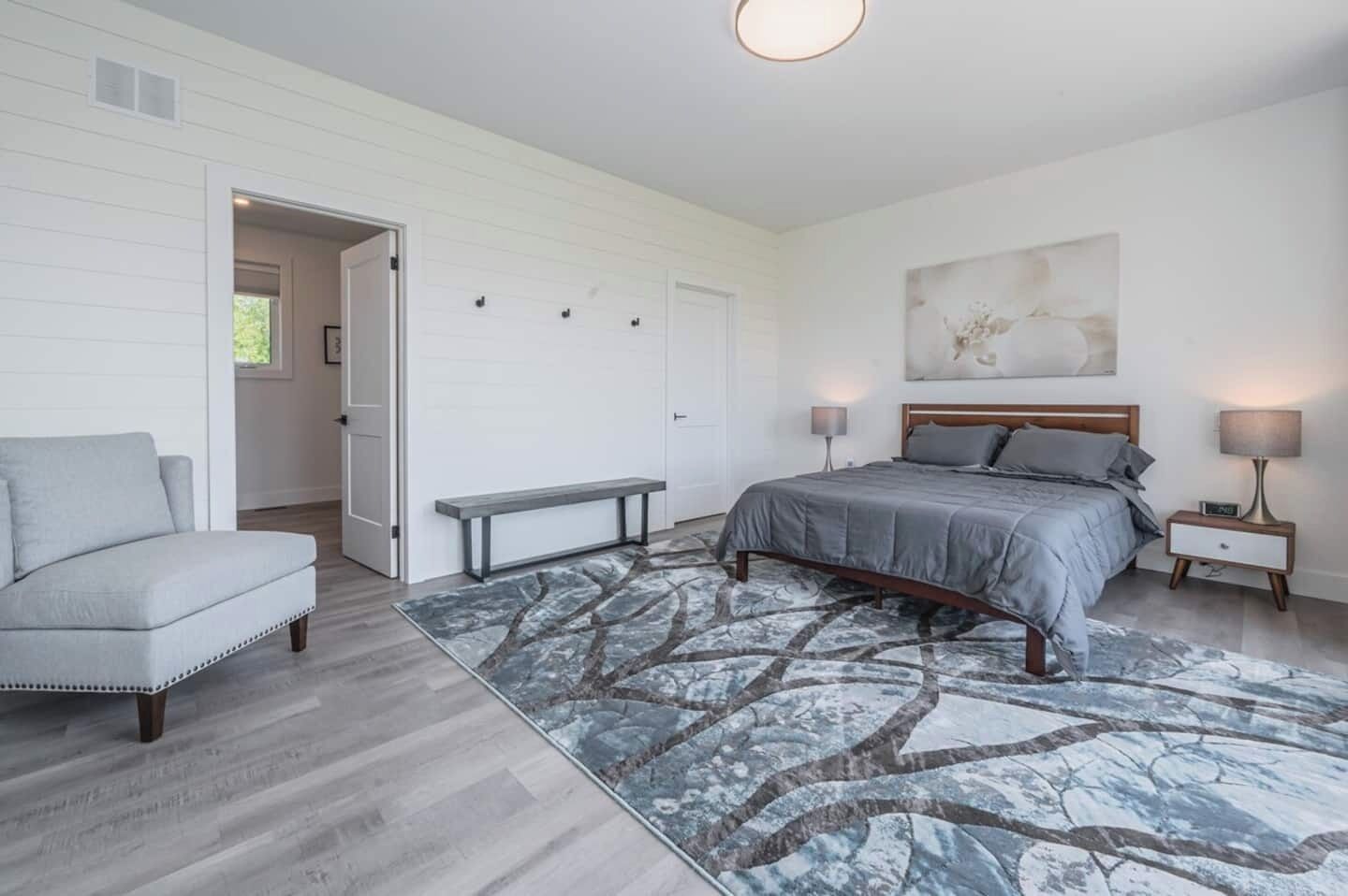 A bedroom with a bed, bench, nightstands, and a painting on the wall.