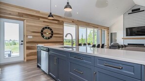 A modern kitchen with a large island, wooden accents, and a view of the outdoors. - Huronia Luxury: Lakefront Views and Game Room (Mar)