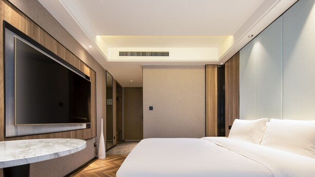 Een moderne hotelkamer met een groot bed, een flatscreen televisie aan de wand en een klein rond tafeltje.