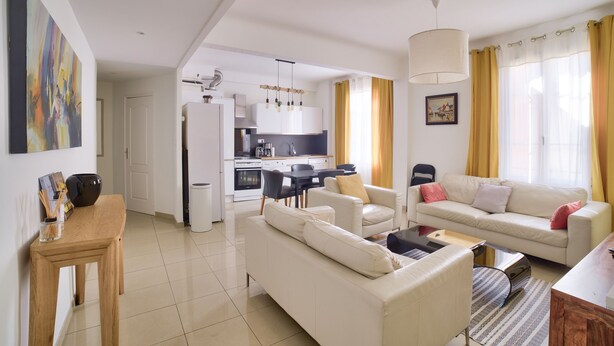 A modern living room with a sofa, coffee table, and dining area. There is a kitchen in the background with white cabinets and a dining table. - Superb Apartment 100 Meters From the Port of Nice (Nice)