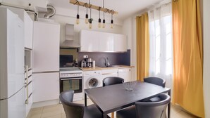 A modern kitchen with white cabinets, a dining table with chairs, and a window with yellow curtains. - Superb Apartment 100 Meters From the Port of Nice (Nice)