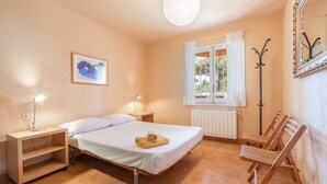A bedroom with a bed, bedside lamps, a radiator, a window with curtains, a coat rack, and a painting on the wall.
