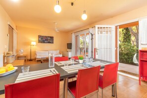 Un coin repas avec une table dressée pour quatre personnes, des chaises rouges, un ventilateur, un téléviseur et un tableau accroché au mur.