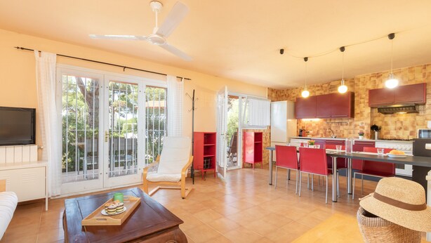A spacious living area with a dining table, a sofa, a TV, and a kitchen with red cabinets and a ceiling fan.