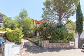 A residential property with a stone wall, a gated entrance, and a pathway leading to a house with a red roof.