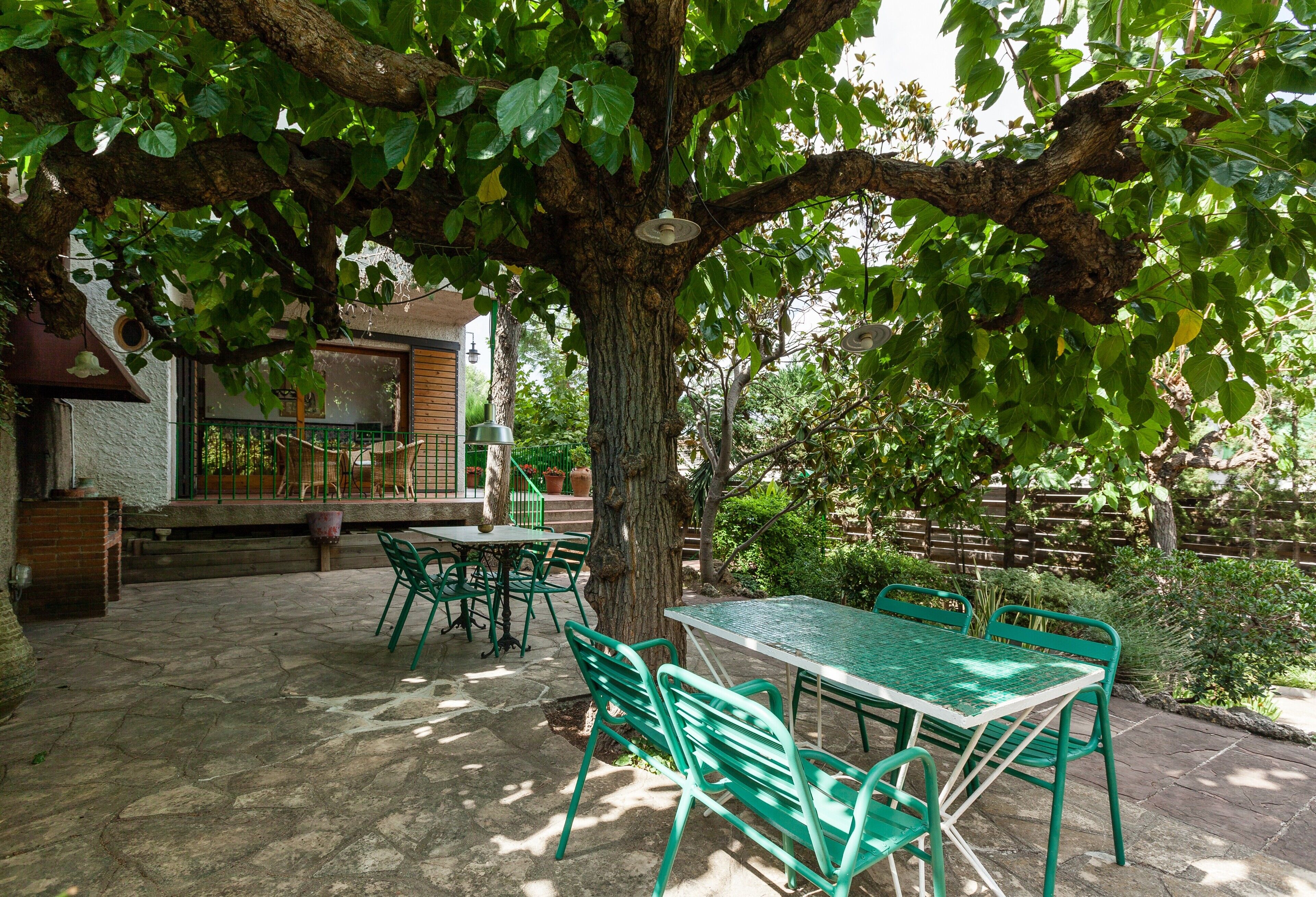 Une terrasse avec une table et des chaises, un arbre, et un bâtiment avec un balcon en arrière-plan.