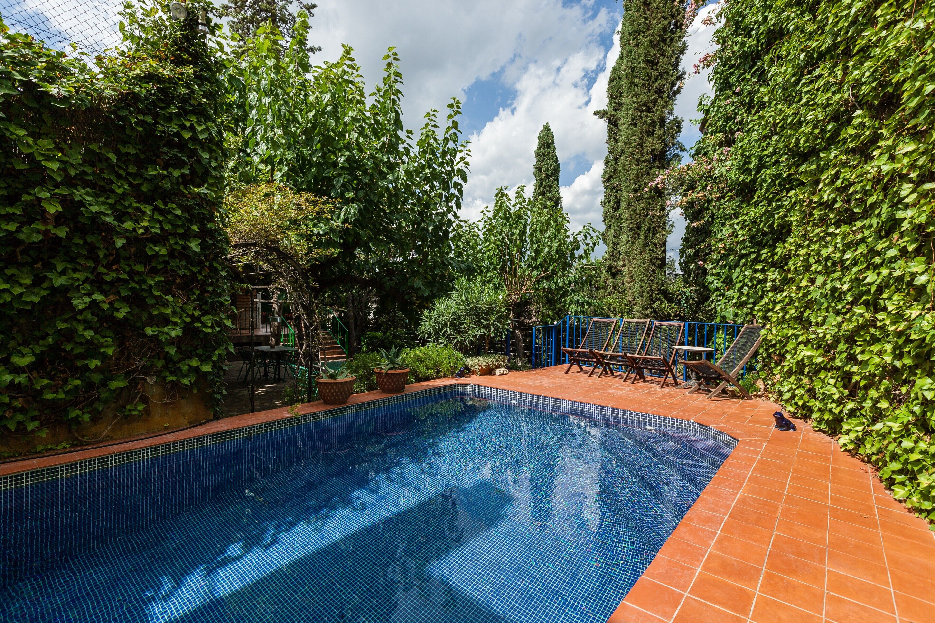 Una piscina rodeada de exuberante vegetación, con solárium de baldosas y mobiliario de exterior.