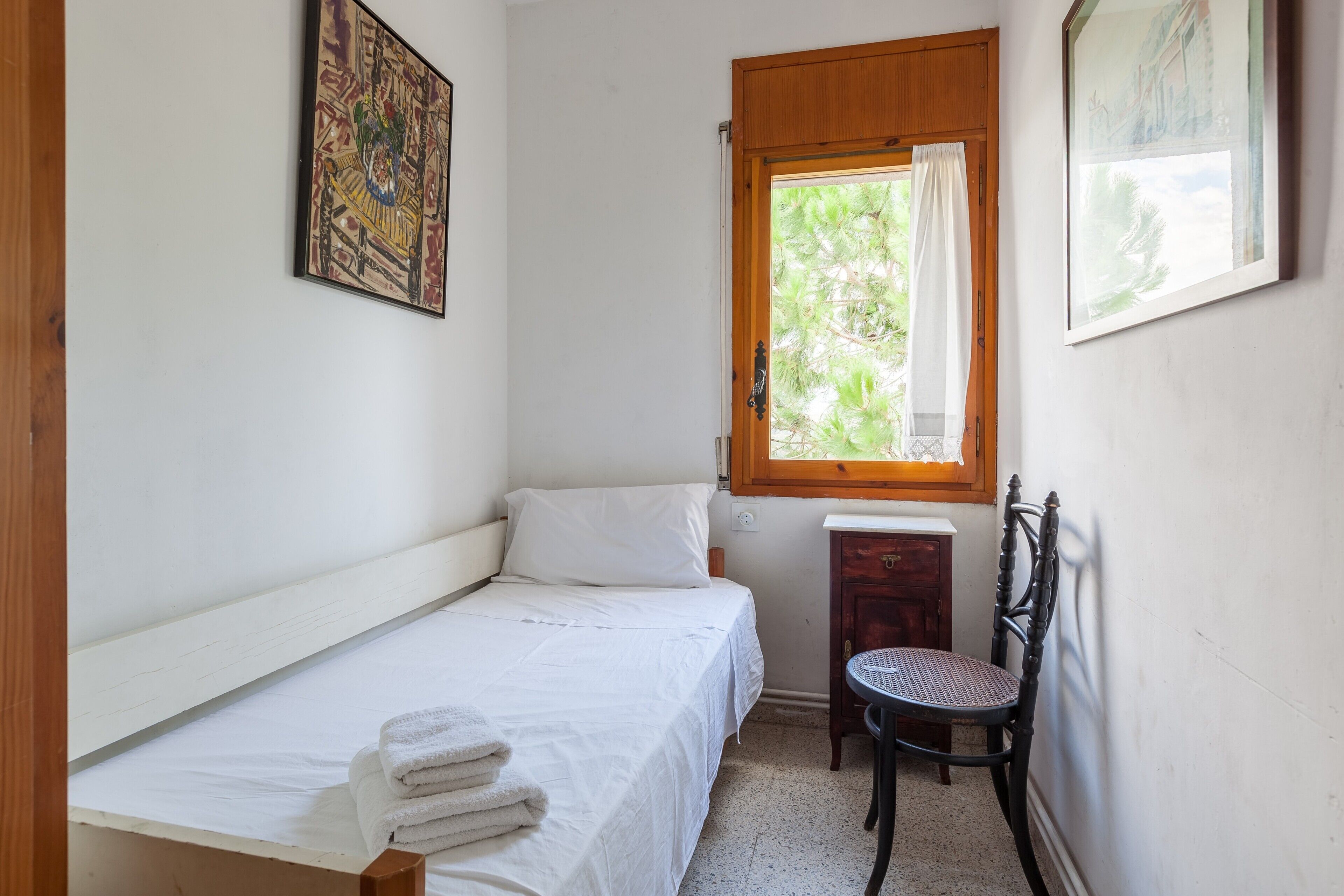 Una habitación pequeña con cama individual, ventana, una silla y una mesita.