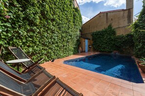 A swimming pool with tiled flooring, a blue door, and a wall covered in green foliage. - Holiday Home 'Can Sebrià' with Mountain View, Pool & Wi-Fi (Gelida)