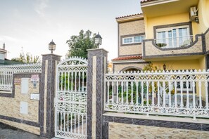 A gated residential area with a stone wall, a metal gate with intricate designs, and a yellow building with a balcony.