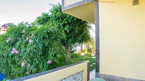 Ein Balkon mit steinernen Brüstungen, einem Tisch mit einer blumigen Tischdecke und üppiger Bepflanzung, darunter blühende Pflanzen.