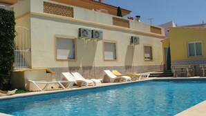 Ein Swimmingpool mit Liegestühlen, Klimaanlagen und einem Gebäude mit einem Ziegeldach.