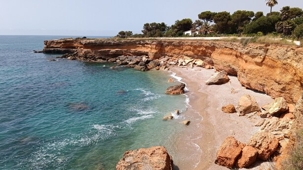 A coastal landscape with clear water, rocky cliffs, and a distant building. - Holiday Apartment Caracola with Balcony, Covered Terrace & Wi-Fi (Vinaròs)