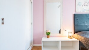 A bedroom with a white console table, a bedside lamp, a bed with a quilted headboard, and a wall-mounted mirror. - Holiday Apartment Caracola with Balcony, Covered Terrace & Wi-Fi (Vinaròs)