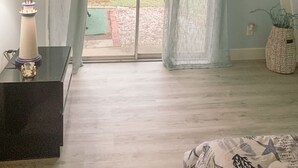 Et værelse med en skydedør, der fører til et udendørs område, et lille bord med en lampe og en potteplante.