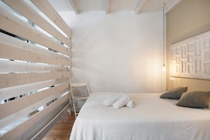 Una camera da letto con un letto, un pannello divisorio in legno a listelli, una sedia bianca e un lampadario a parete.