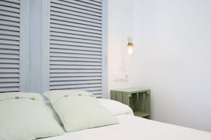 Un dormitorio con cama, almohadas, una mesita de noche y una lámpara de pared.