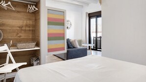 Een moderne slaapkamer met een bed, een zithoek met een bank, een houten garderobe en een kleurrijke gestreepte wand.