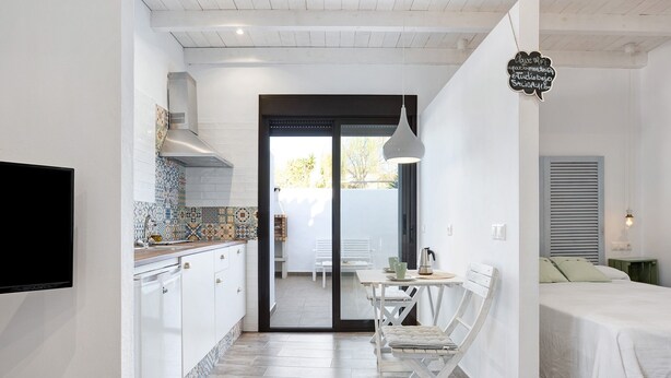Een moderne keuken met witte kasten, een betegelde achterwand en een eethoek met een witte tafel en stoelen.
