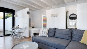 Een moderne woonkamer met een grijze bank, een ronde salontafel met een stershaped ontwerp, en een eethoek met een witte tafel en stoelen.