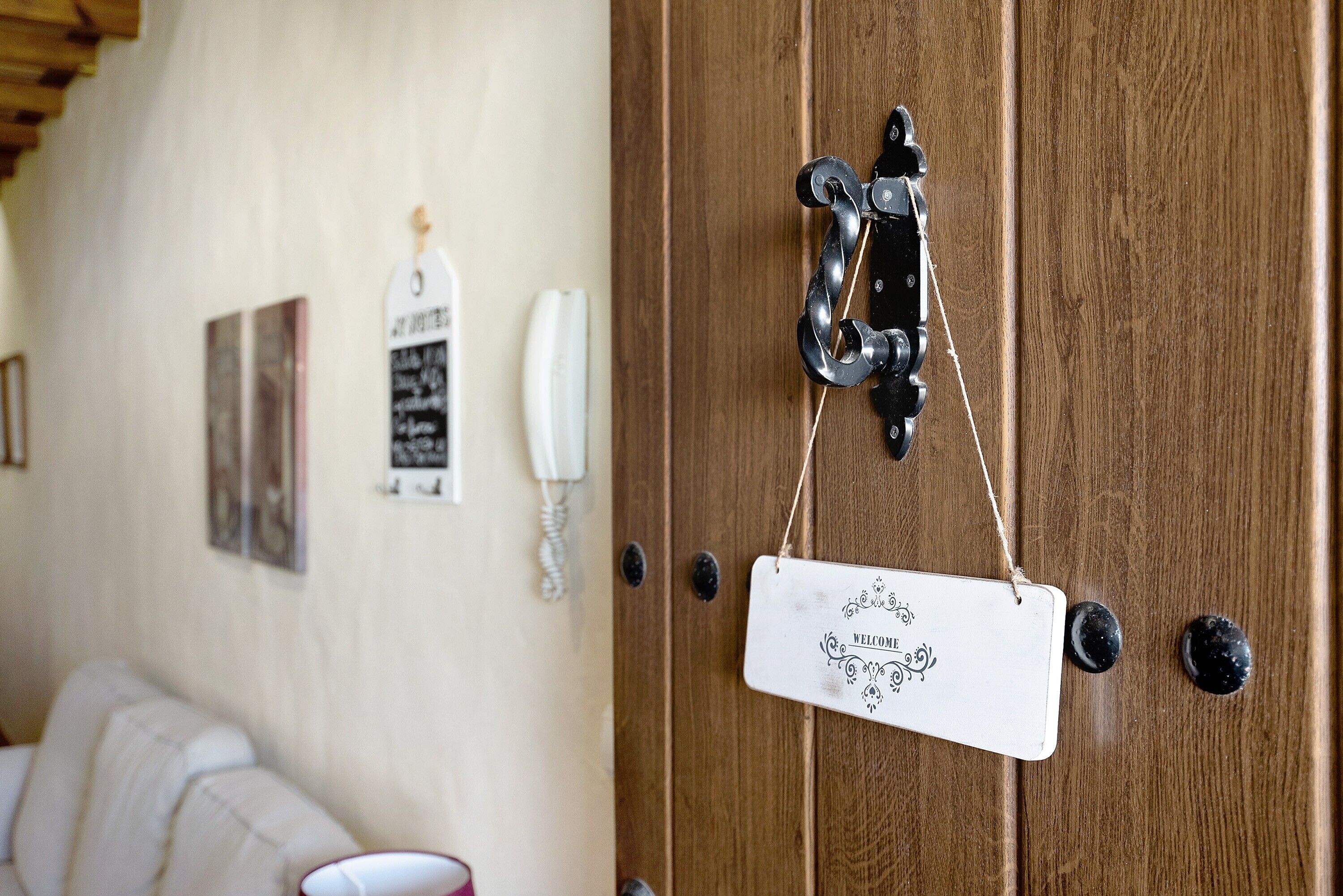 A wooden door with a metal handle, a white sign with 'WELCOME' written on it, and a small white object hanging from the door.