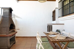 A patio with a stone oven, a table set for dining, and a window with a metal grill.