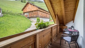 A wooden balcony with a view of a mountain house, a table with chairs, and a potted plant. - 'Bolser Apartment Plan de Corones' with Mountain View, Garden & Wi-Fi (Pieve di Marebbe)