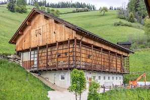 A wooden chalet with a balcony, set on a hillside with a gravel path leading to it.