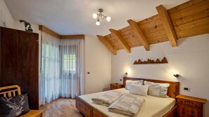 Ein Schlafzimmer mit einem hölzernen Bett, einem Nachttisch, einer Bank und einer Decke mit sichtbaren Balken.