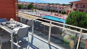 En balkong med ett bord dukat för frukost, med utsikt över en swimmingpool och bostadshus.