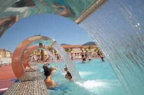 A swimming pool with a water feature, surrounded by buildings and palm trees.