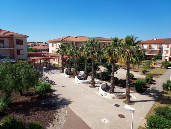 A courtyard with palm trees, a covered seating area, and buildings with red-tiled roofs.