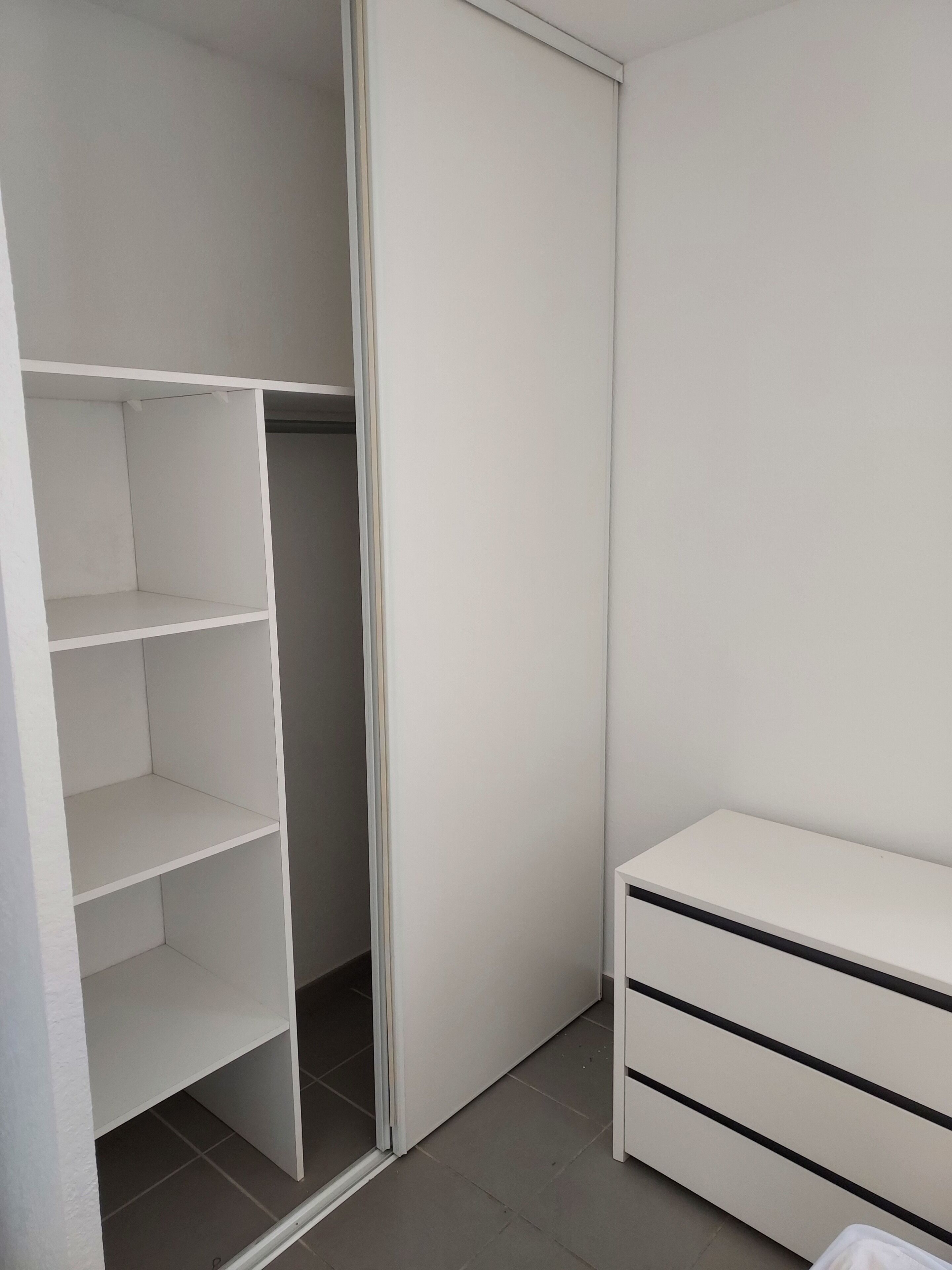 Un placard blanc avec des étagères ouvertes et une porte fermée.