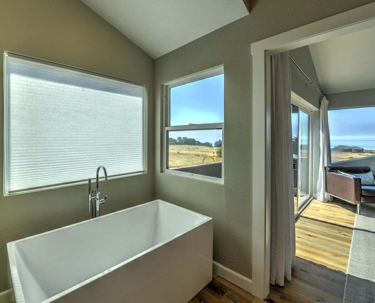 Une salle de bain moderne avec une baignoire sur pieds, de grandes fenêtres et une vue sur l’extérieur.