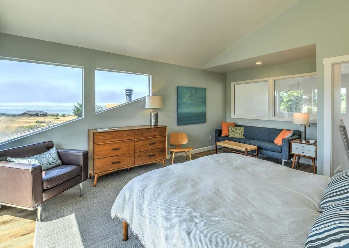 A bedroom with a large bed, a dresser, a sofa, and a view of the ocean.