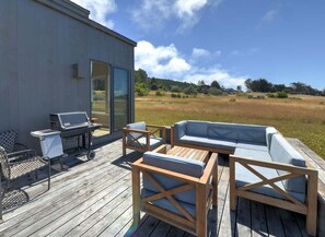 An outdoor deck with a grill, seating, and a view of a field. - Lovely Day | BBQ Grill, Hot Tub, & Ocean Views (Sea Ranch)