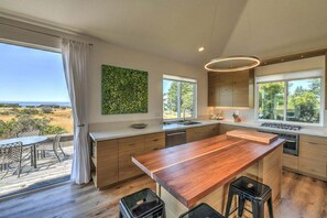 A modern kitchen with a large island, wooden countertops, and a view of the outdoors. - Lovely Day | BBQ Grill, Hot Tub, & Ocean Views (Sea Ranch)