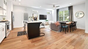 A modern kitchen with white cabinets, a central island, and a dining area with a grey sofa and black chairs.