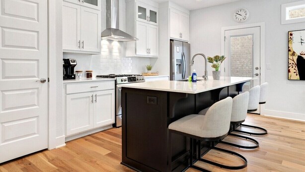 A modern kitchen with white cabinets, a central island with bar stools, a stainless steel refrigerator, and a built-in oven.