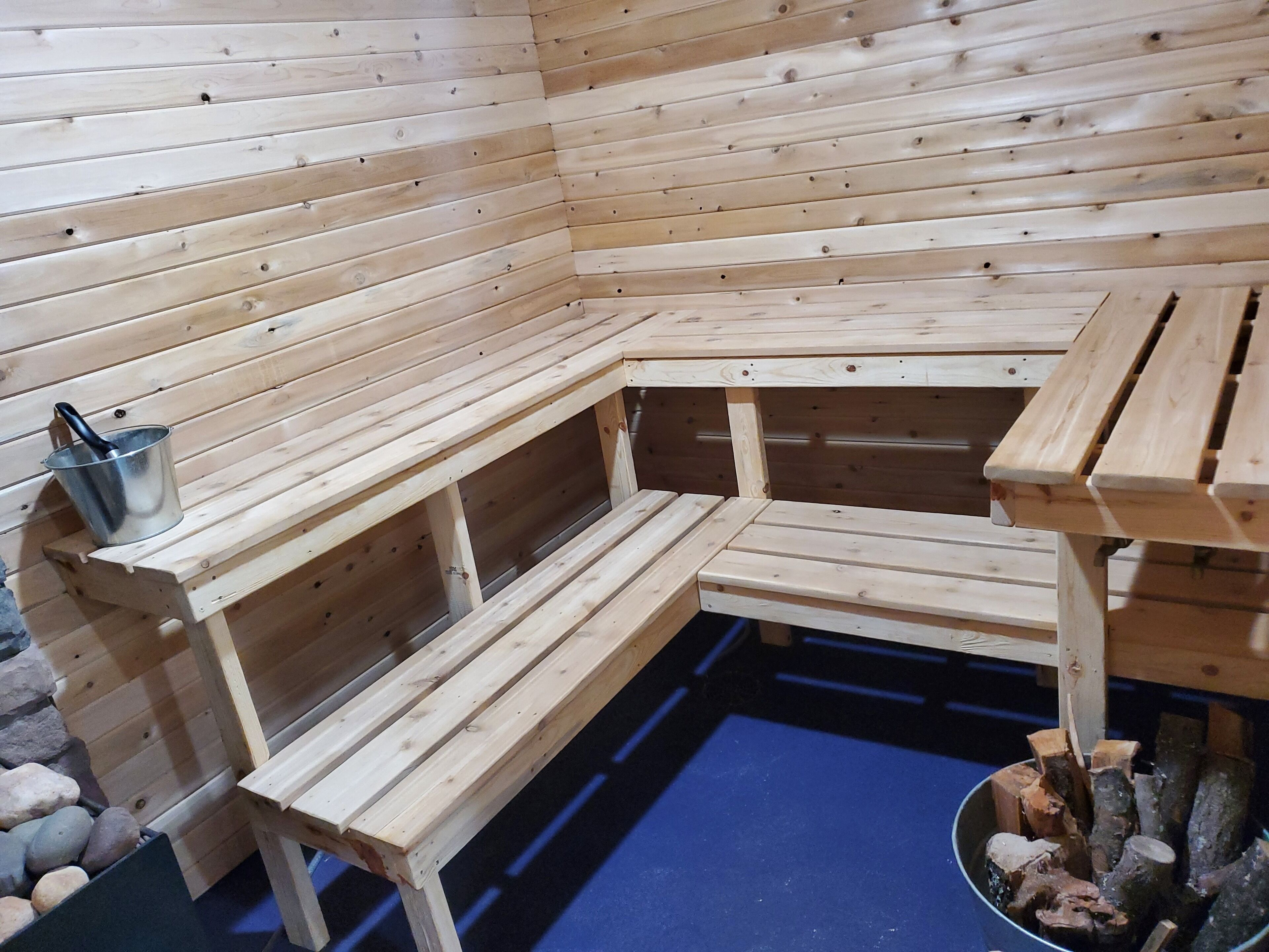 En träbeklädd bastu med sittbänkar och en metallhink.
