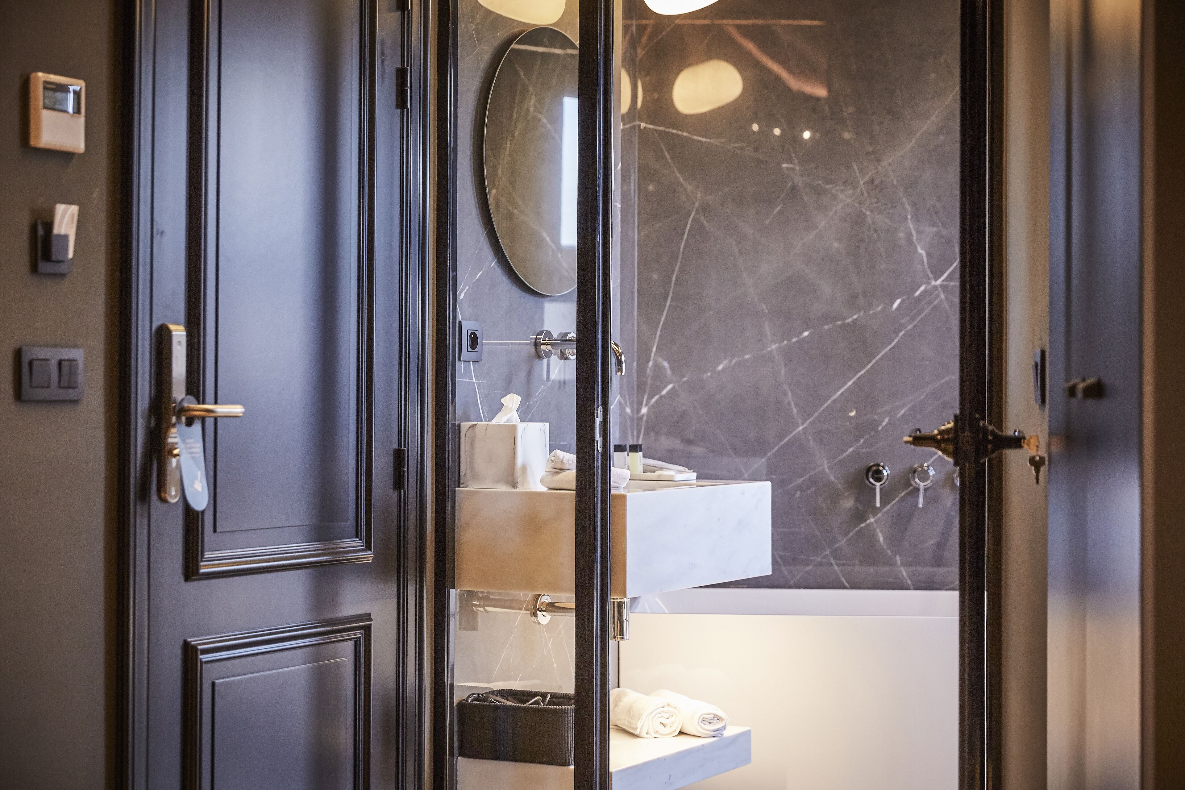 Une salle de bain moderne avec un mur en marbre, un miroir rond et un porte-serviettes.