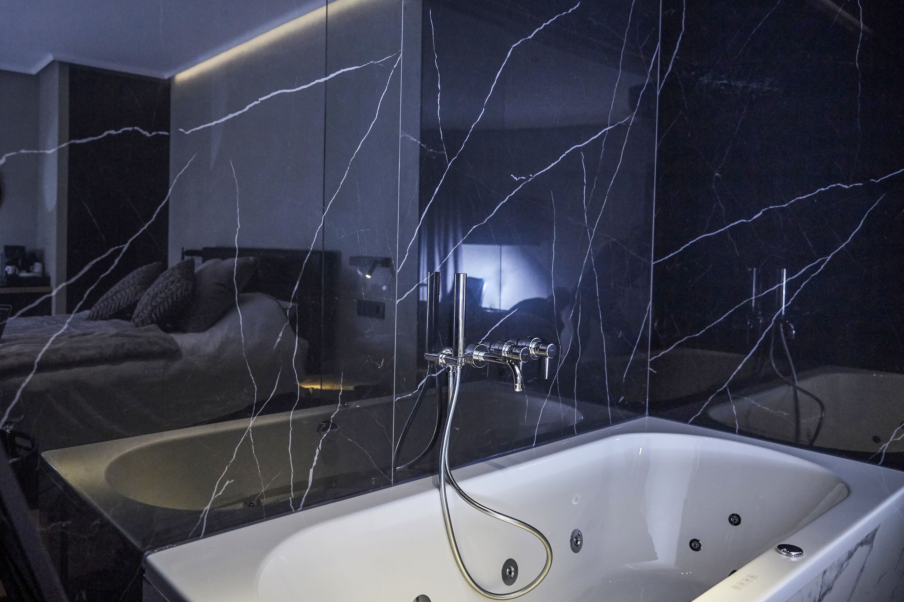 Ein modernes Badezimmer mit einer gläsernen Badewanne, sichtbaren Wasserlinien und einer dunkel marmorierten Spritzschutzeinrichtung.