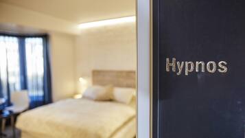 A hotel room with a bed, a chair, and a desk. The room has a sign that says "Hypnos".