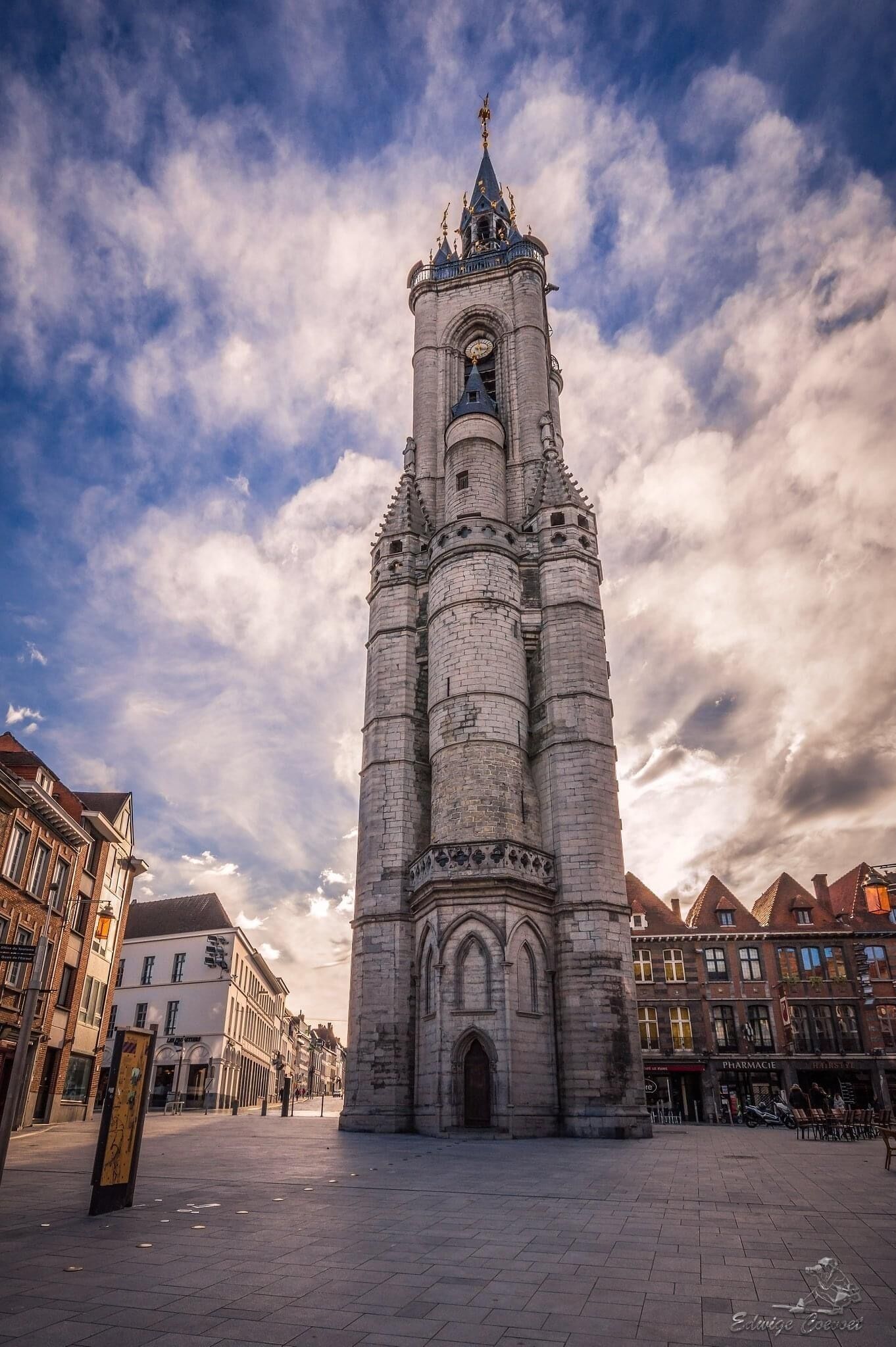 A historic tower with a clock, surrounded by buildings and a paved square.