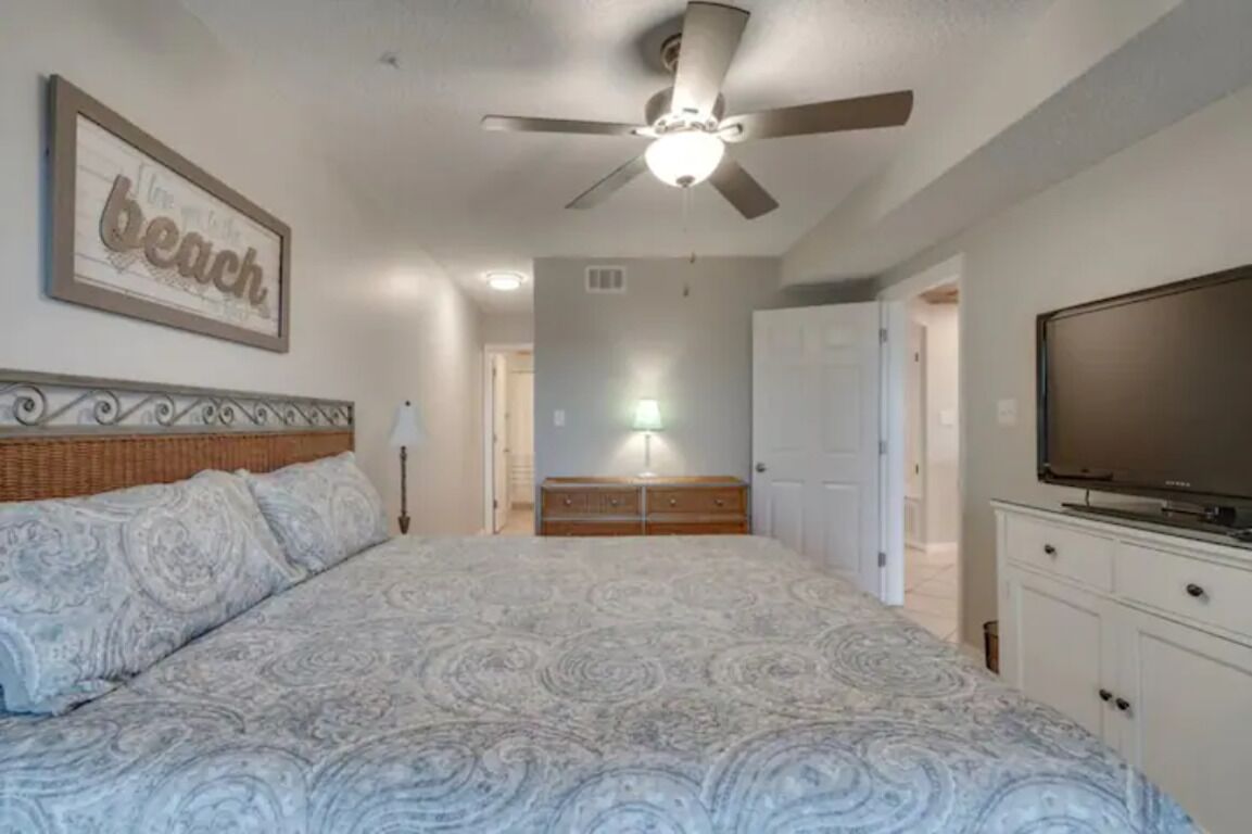 A bedroom with a large bed, a ceiling fan, a TV, and a dresser.