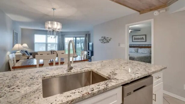 A modern kitchen with a granite countertop, stainless steel sink, and a dining area with a white table and chairs.