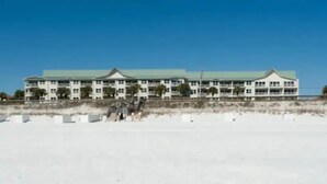 A large, multi-story hotel with a green roof and white exterior walls, located near a beach.