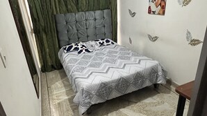 A small, well-lit bedroom with a bed, a headboard, a wall with decorative leaf patterns, and a door with curtains. - Come to me (Cali)
